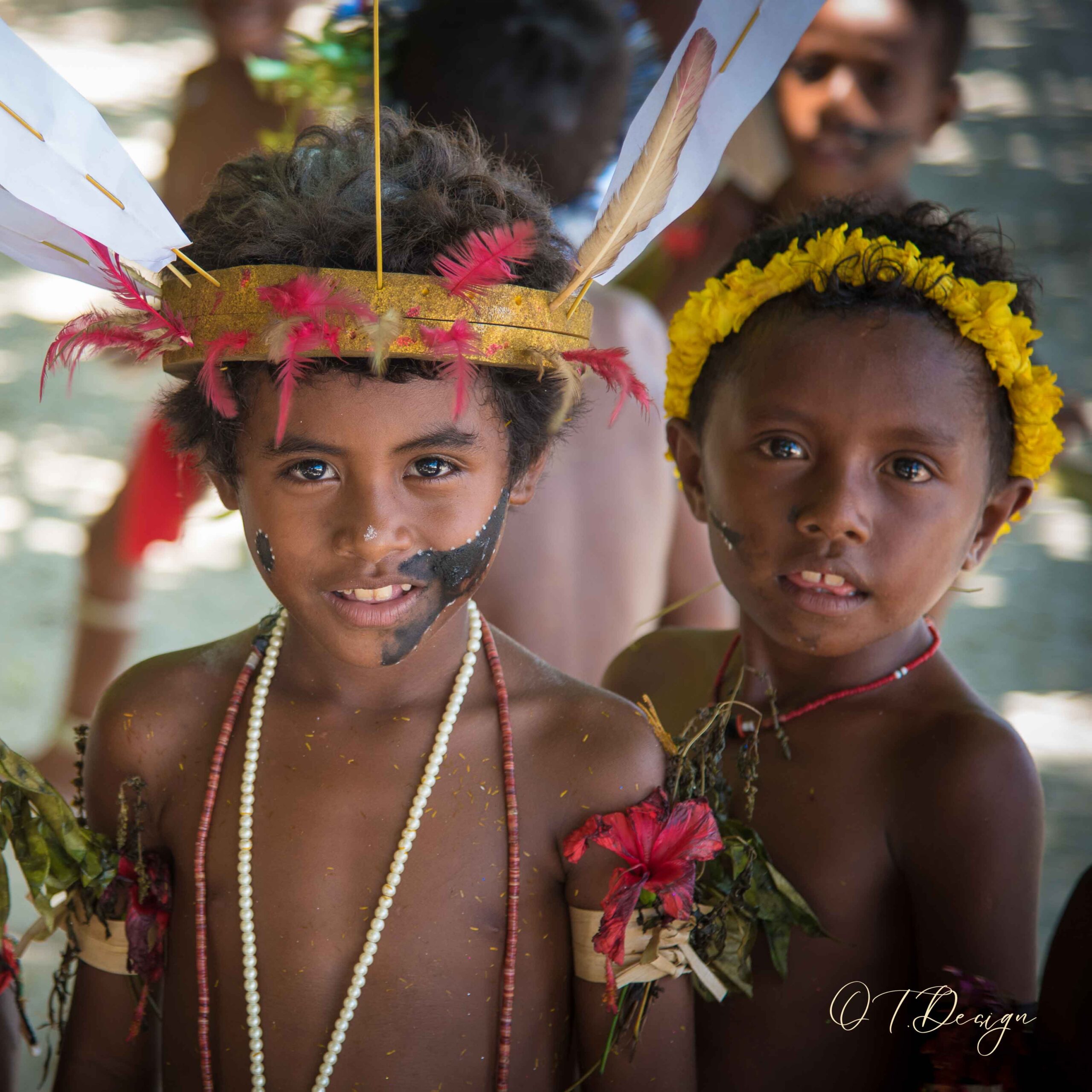 Two local kids wearing traditional accessories, such as pearls and feathers to their heads and necks, in Kitava Island, Papua New Guinea