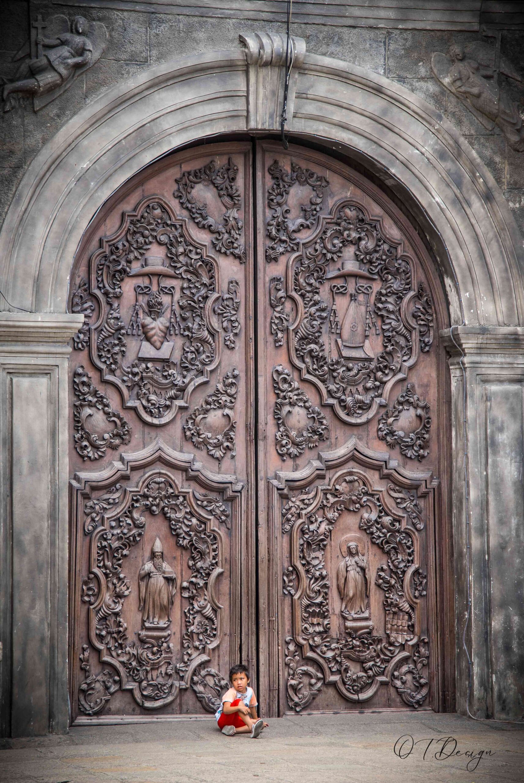 A very small kid in front of a majestic door in Manila, Philippines