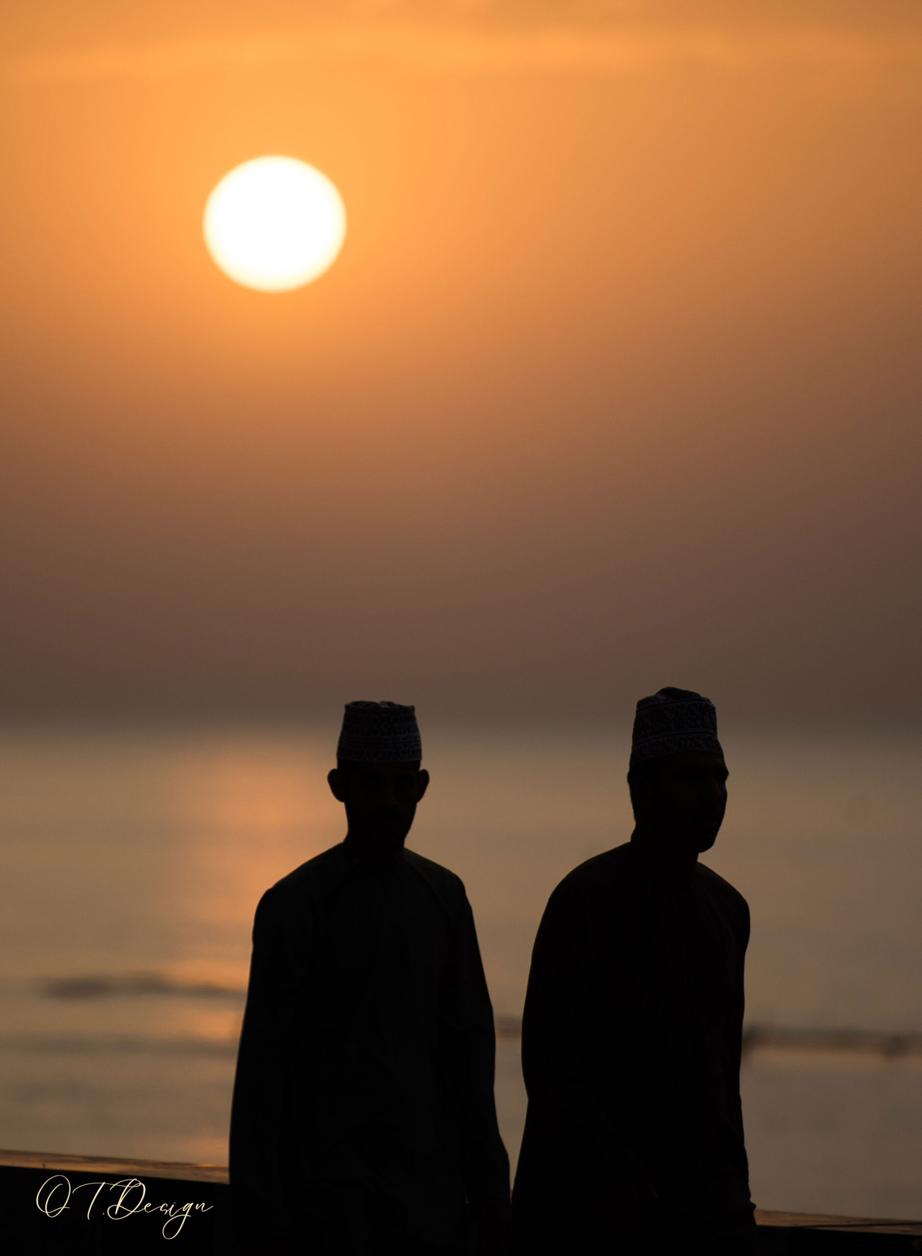 Silhouettes of two men walking on the beach at sunset in Muscat, Oman